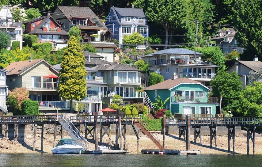 Nestled in charming neighborhoods, houses perch on a hillside overlooking a tranquil body of water in Vancouver, complete with docks and a serene boat in the foreground.