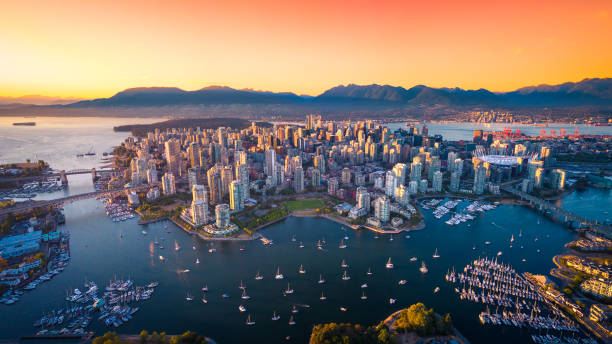 Aerial view of Vancouver's city skyline with mountains in the background, numerous boats in the harbor, and a vibrant sunset sky. Perfect for homebuyers seeking breathtaking vistas.