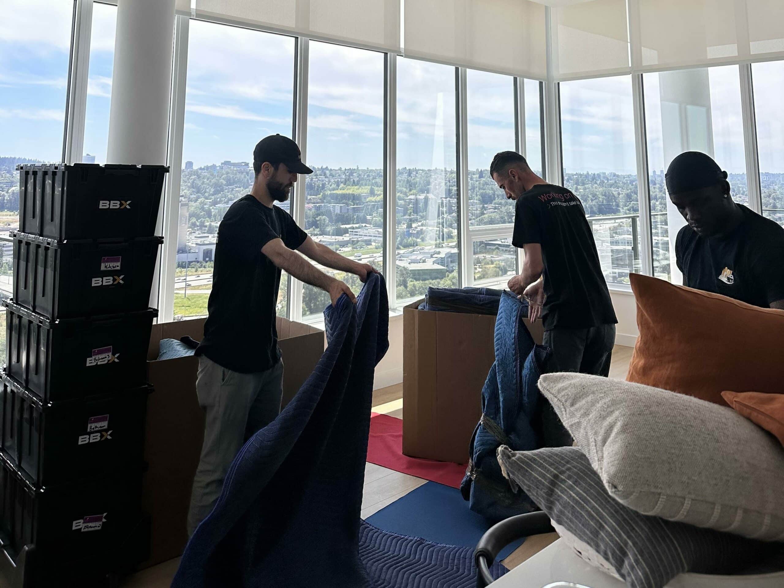 Three people are unpacking and organizing boxes in a spacious room with tall windows and a stunning city view, following a comprehensive moving checklist to ensure everything is perfectly in place.