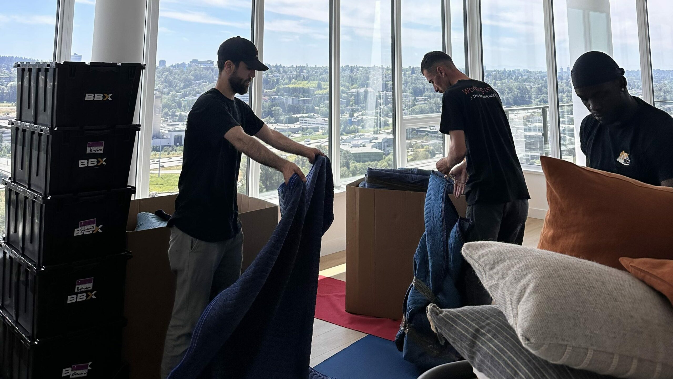 BBX movers team. As boxes, cushions, and blankets are organized, the cityscape outside offers a serene backdrop. They're working from a comprehensive moving checklist to ensure everything goes smoothly.