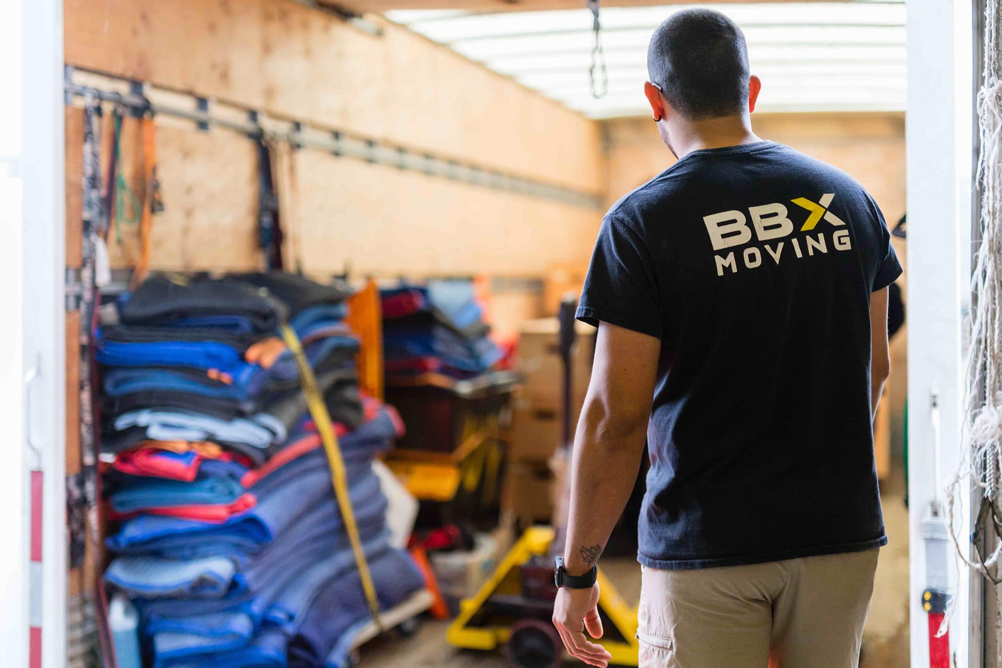 BBX Moving | Locations - A person wearing a "BBX Moving" shirt stands inside a moving truck filled with folded blankets and moving equipment, ready to assist as trusted office movers in Richmond. A person wearing a "BBX Moving" shirt stands inside a moving truck filled with folded blankets and moving equipment, ready to assist as trusted office movers in Richmond.