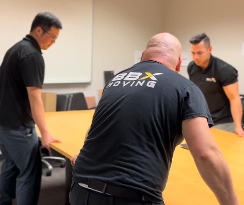 BBX Moving | Office Movers – Burnaby - Three men from Office Movers are moving a large wooden table in a Richmond office setting. Three men from Office Movers are moving a large wooden table in a Richmond office setting.