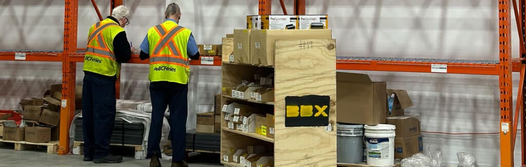 BBX Moving | Commercial Movers – Burnaby - Two workers in safety vests organize and check inventory on shelves in a Richmond warehouse, showcasing the efficiency of experienced commercial movers with boxes and supplies. Two workers in safety vests organize and check inventory on shelves in a Richmond warehouse, showcasing the efficiency of experienced commercial movers with boxes and supplies.