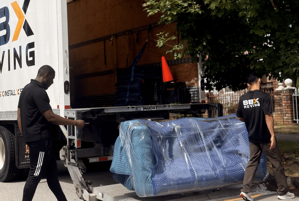BBX Moving | How to Prepare Furniture for Moving: A Practical Step-by-Step Guide - Two movers load a large, wrapped item onto a BOX MOVING truck using a ramp; the team expertly handles furniture moving and uses proper equipment inside to prepare furniture for safe transport. Two BBX movers load a large, wrapped item onto a BBX MOVING truck using a ramp; the team expertly handles furniture moving and uses proper equipment inside to prepare furniture for safe transport.