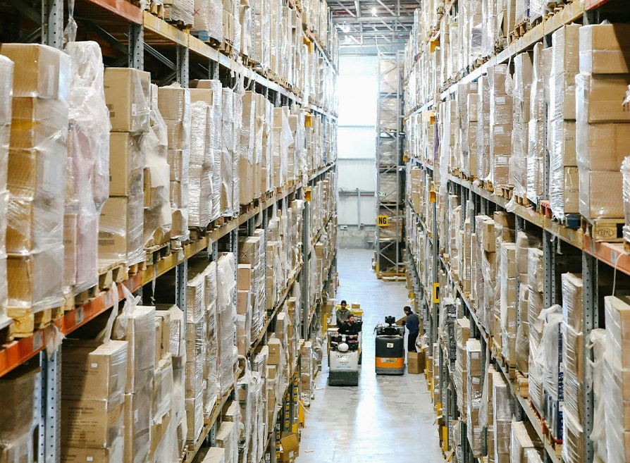 BBX Moving | Warehouse Movers – West Vancouver - Large warehouse in Richmond with tall shelves stacked with boxes and pallets; Warehouse Movers and forklifts are seen operating in the central aisle. Large warehouse in Richmond with tall shelves stacked with boxes and pallets; Warehouse Movers and forklifts are seen operating in the central aisle.